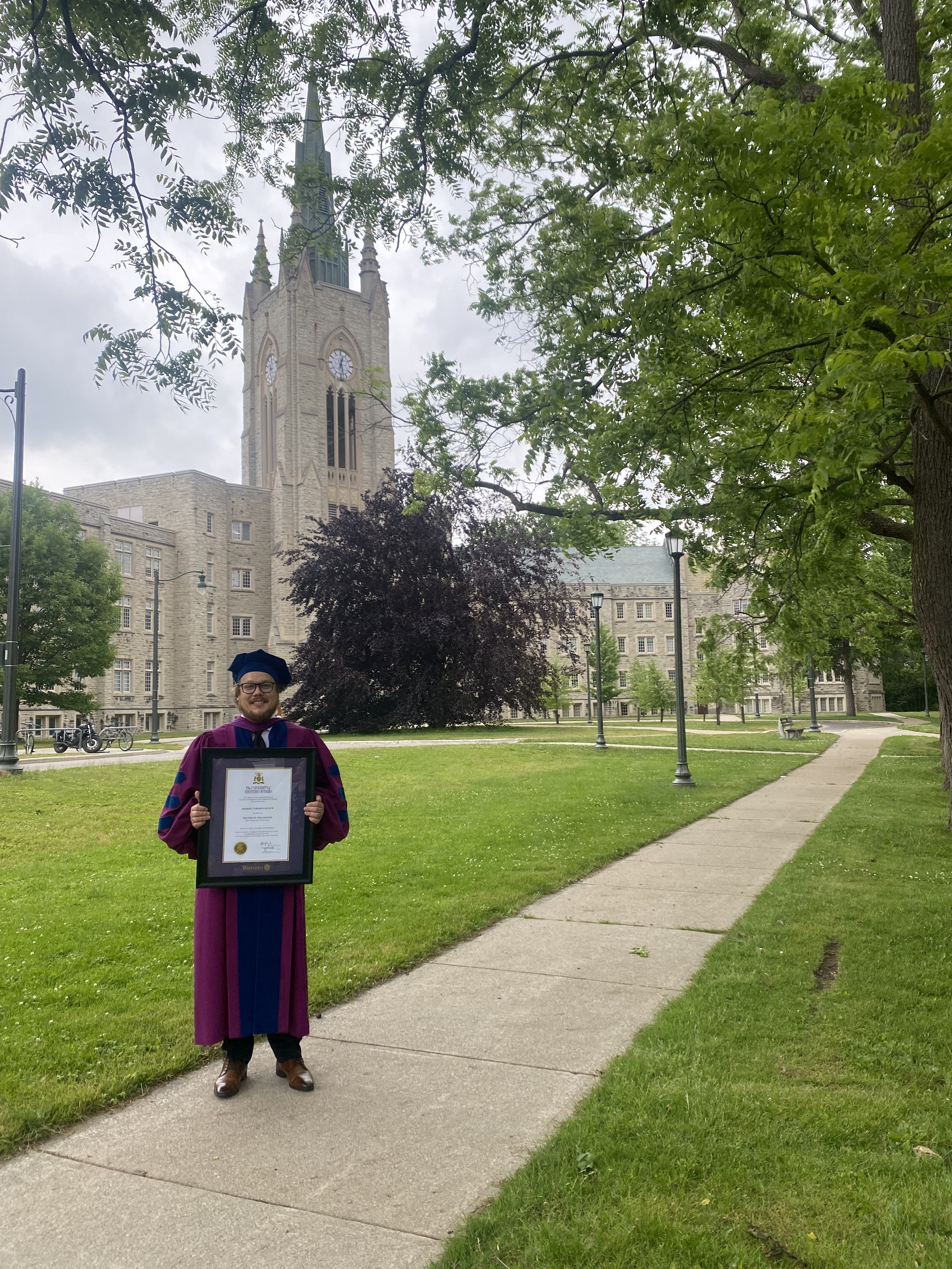 Robert Kuiack in doctoral regalia with his Ph.D. diploma on Western's campus